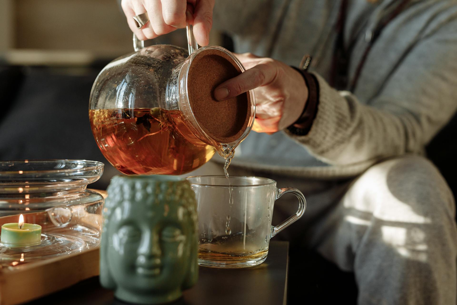 A person pouring herbal tea into a cup by candlelight creating a warm atmosphere for intuitive practice