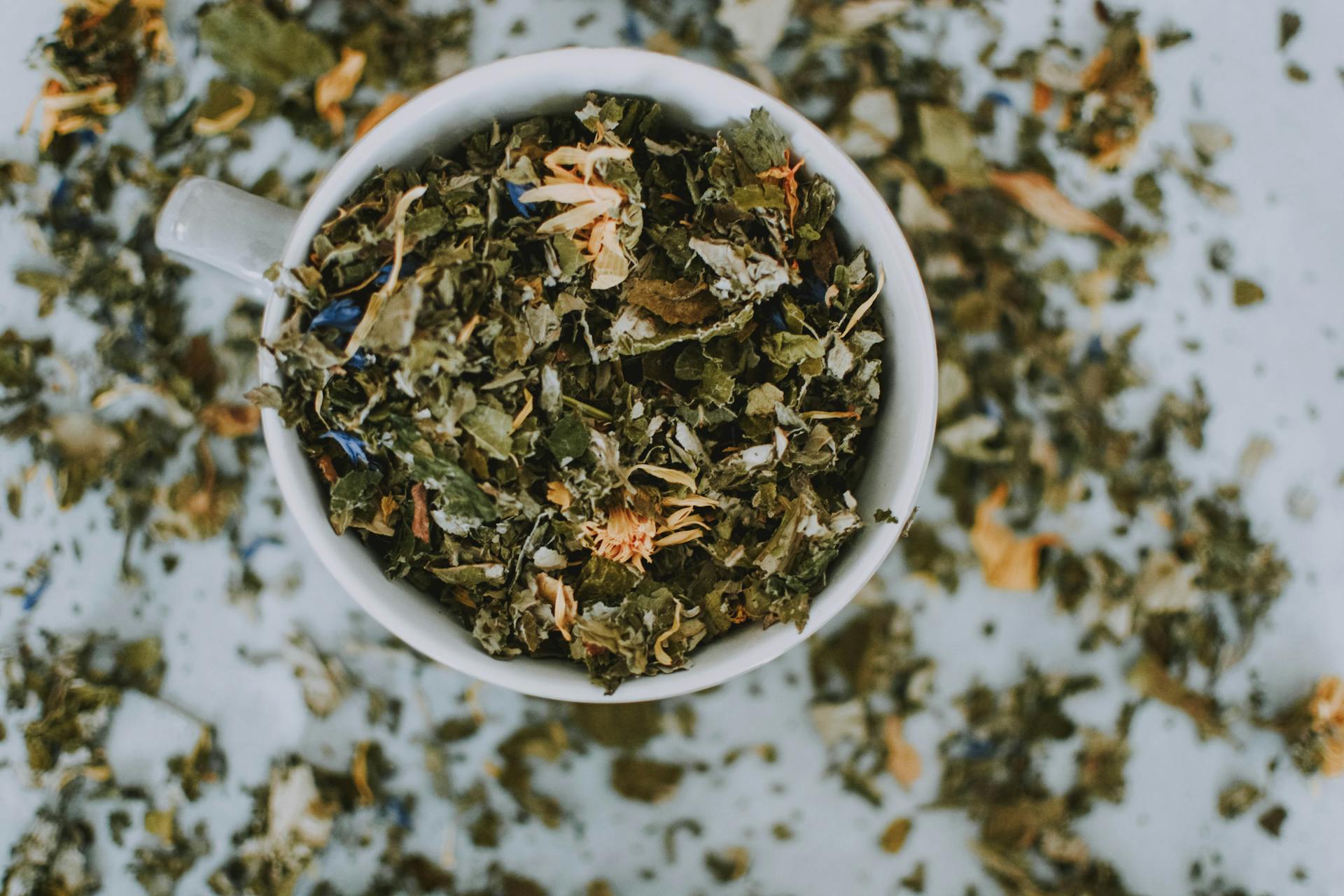 Overhead view of dried herbal tea leaves and flowers inside a cup representing the raw materials of tasseography