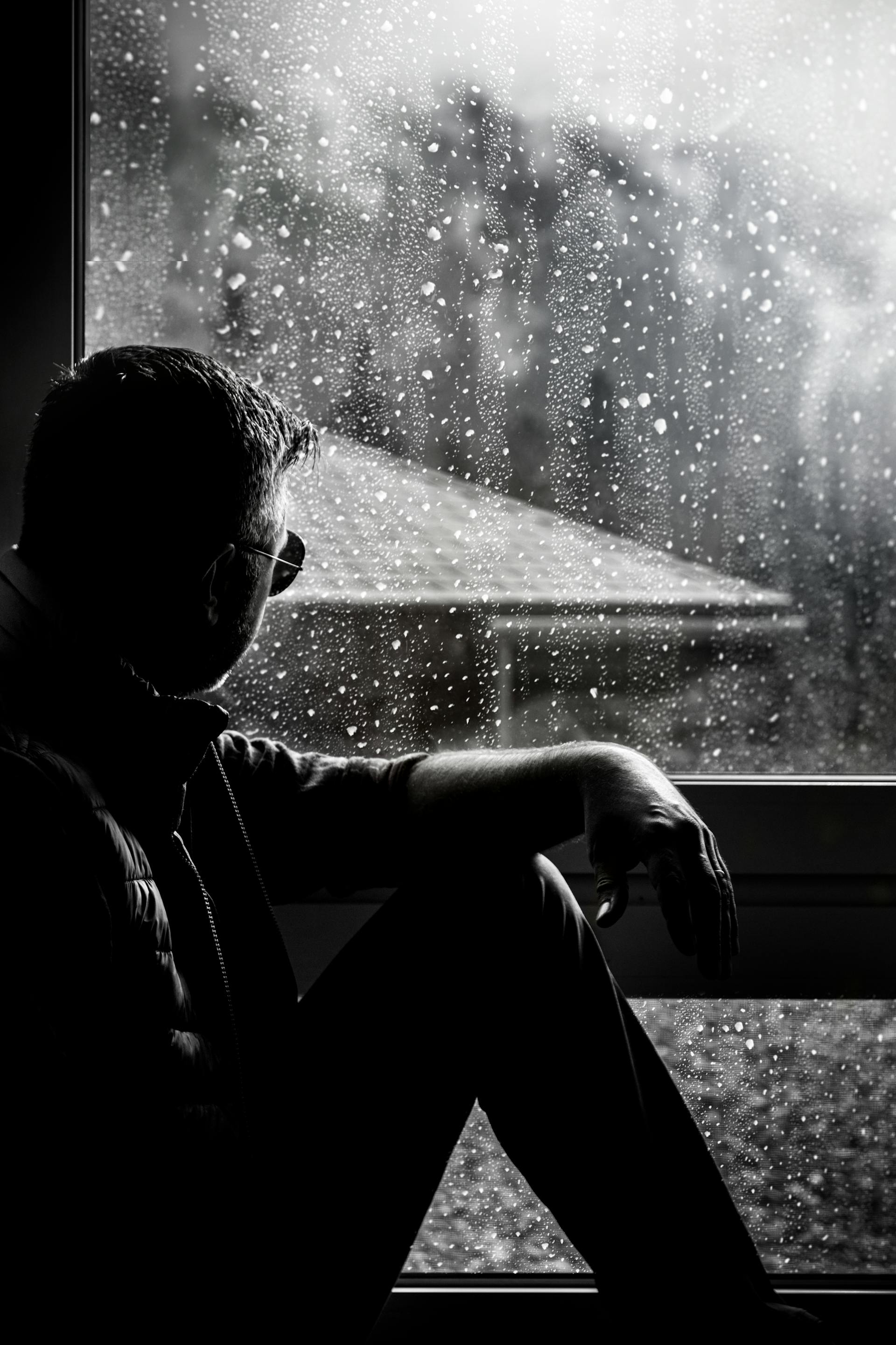 A silhouette sitting by a rainy window deep in thought capturing the solitary grief and inner storm of the Three of Swords