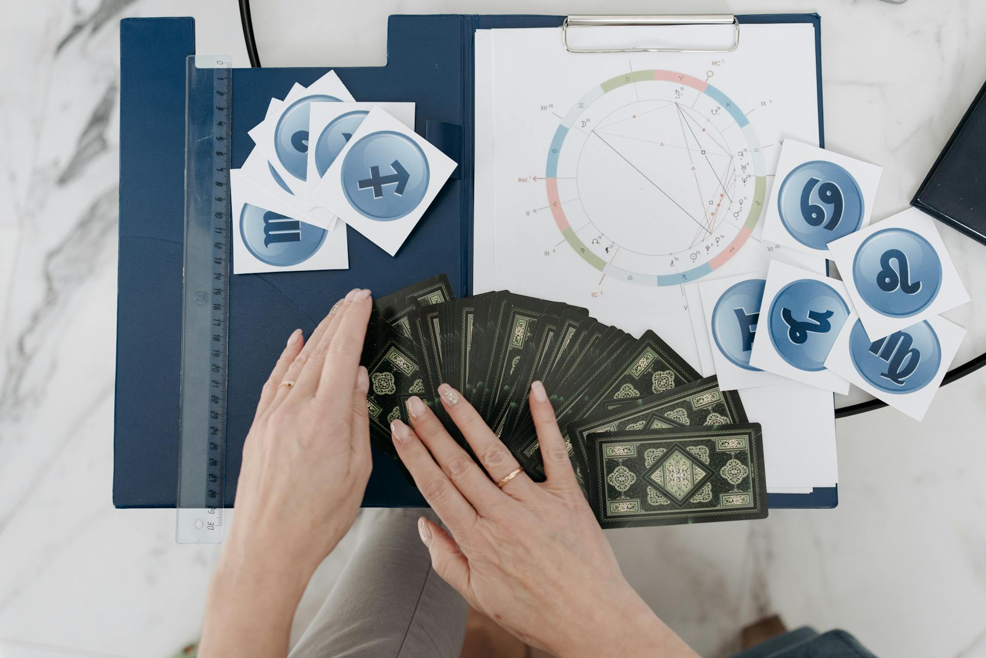 Hands arranging tarot cards with astrology symbols and natal chart on a table for relationship chart reading