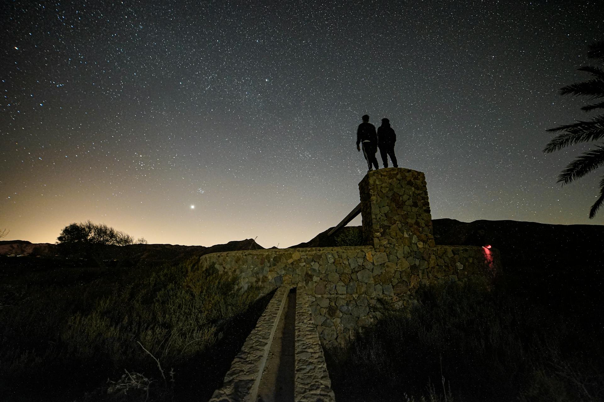 Silhouettes of two people under a starry night sky creating a dramatic scene of connection and destiny