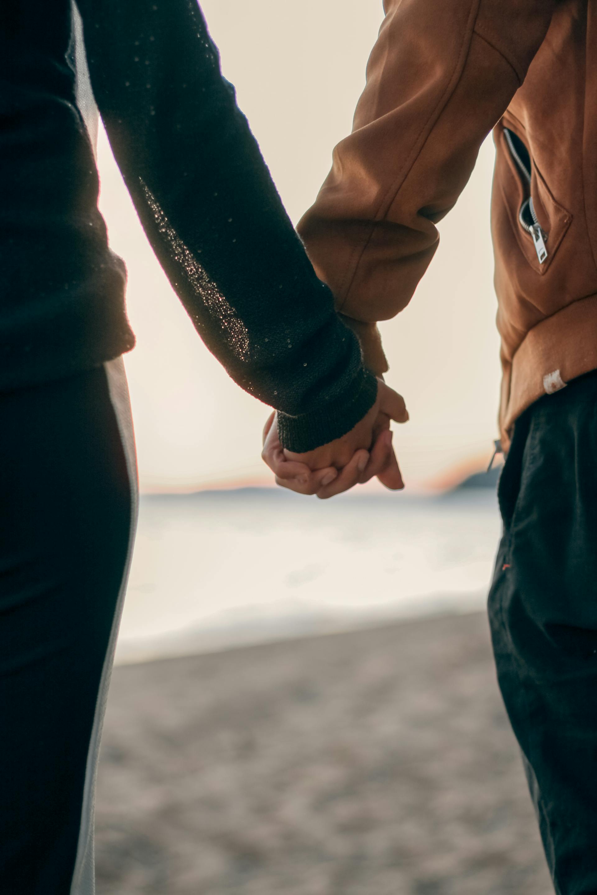 A couple holds hands during a romantic walk on the beach at sunset symbolizing deep connection and love