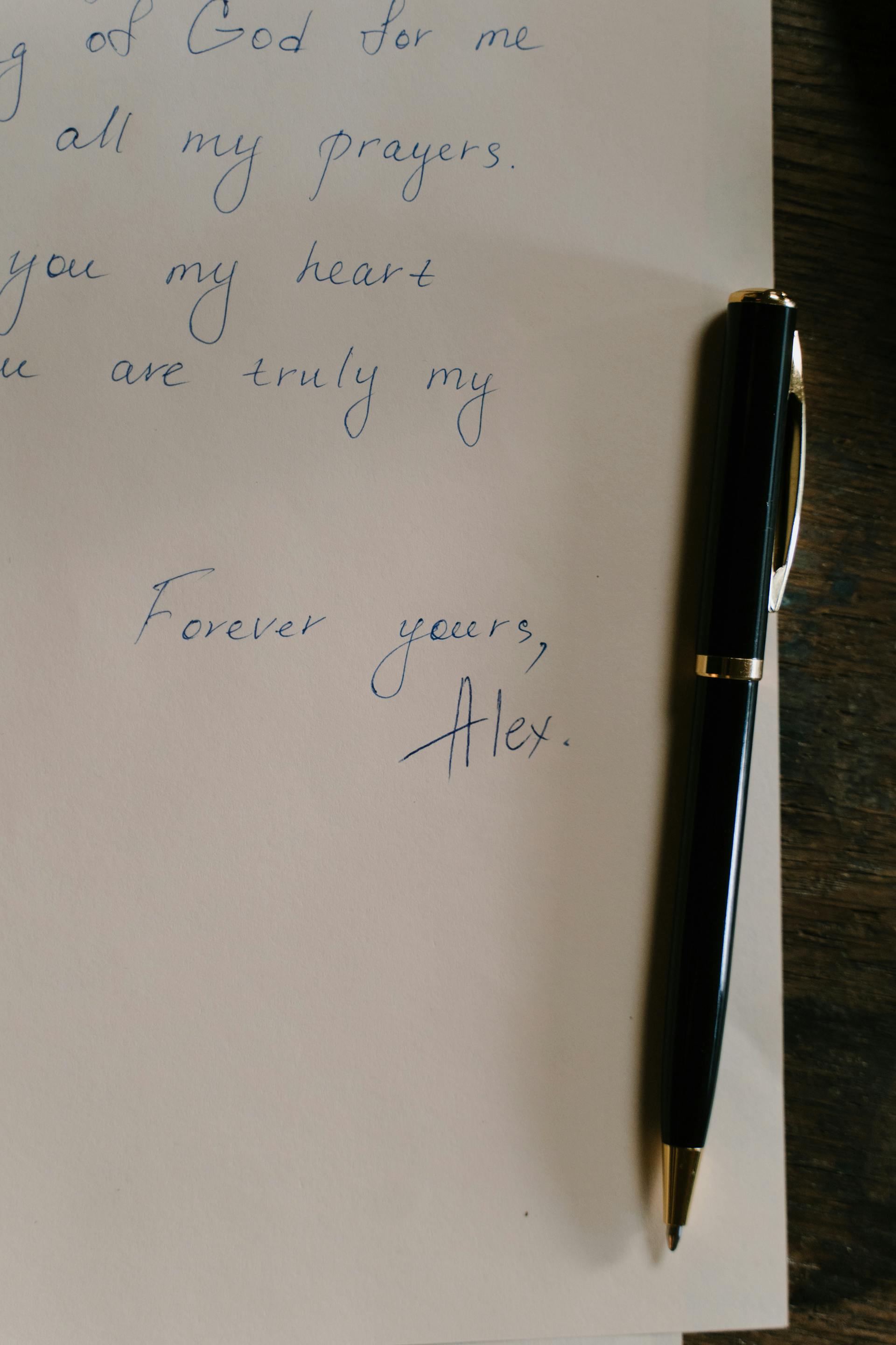 A close-up of a handwritten letter with a pen on a wooden desk conveying personal sentiments and devotion